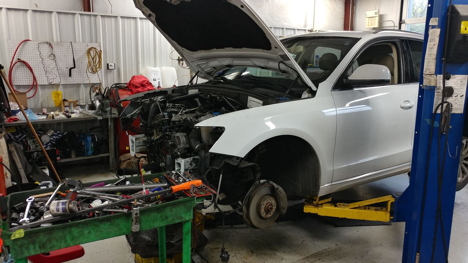 A white car with the hood up is sitting on a lift in a garage. | Import Specialty Service