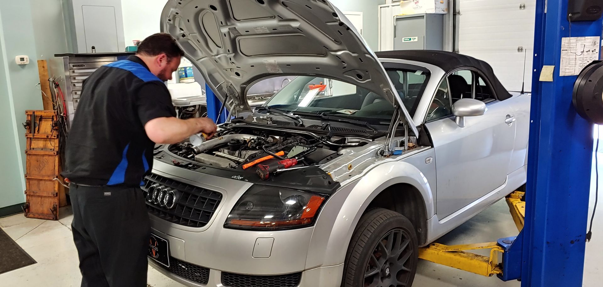 A man is working on a car with the hood open in a garage. | Import Specialty Service | Import Specialty Service
