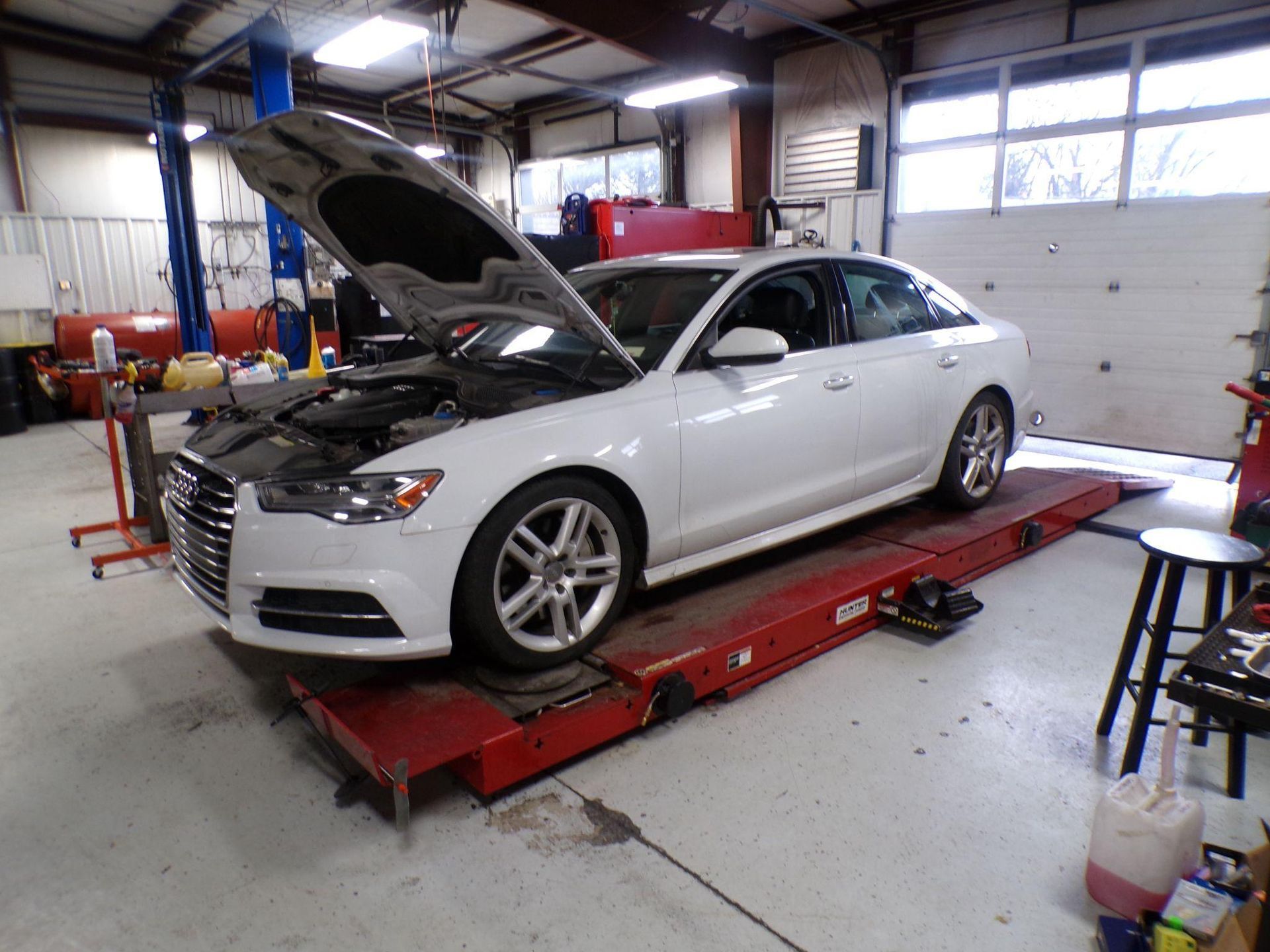 A white car with the hood up is on a lift in a garage. | Import Specialty Service