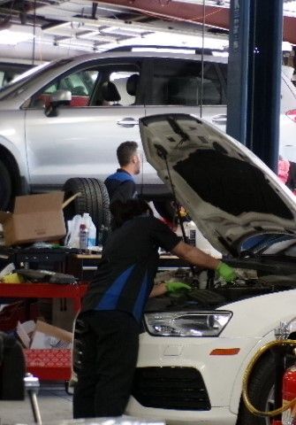 A man is working on a car with the hood open in a garage. | Import Specialty Service