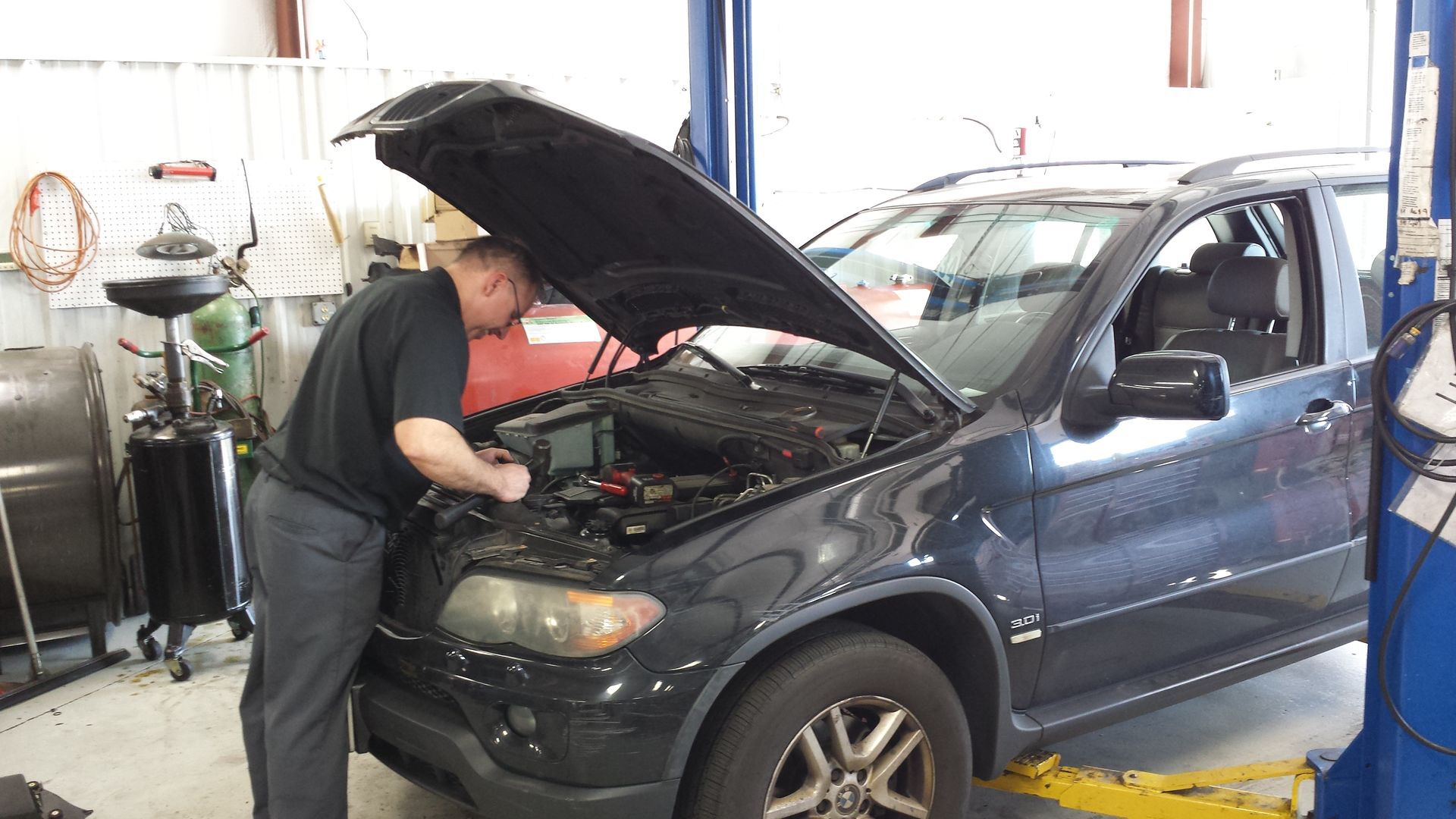A man is working on a car in a garage with the hood open. | Import Specialty Service