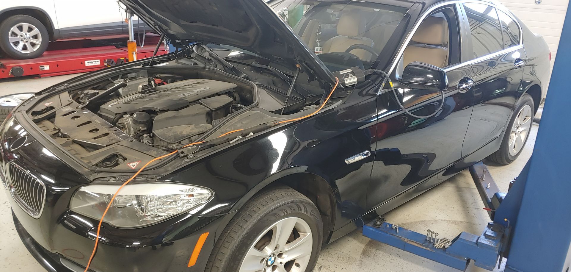 A black car with the hood up is on a lift in a garage. | Import Specialty Service
