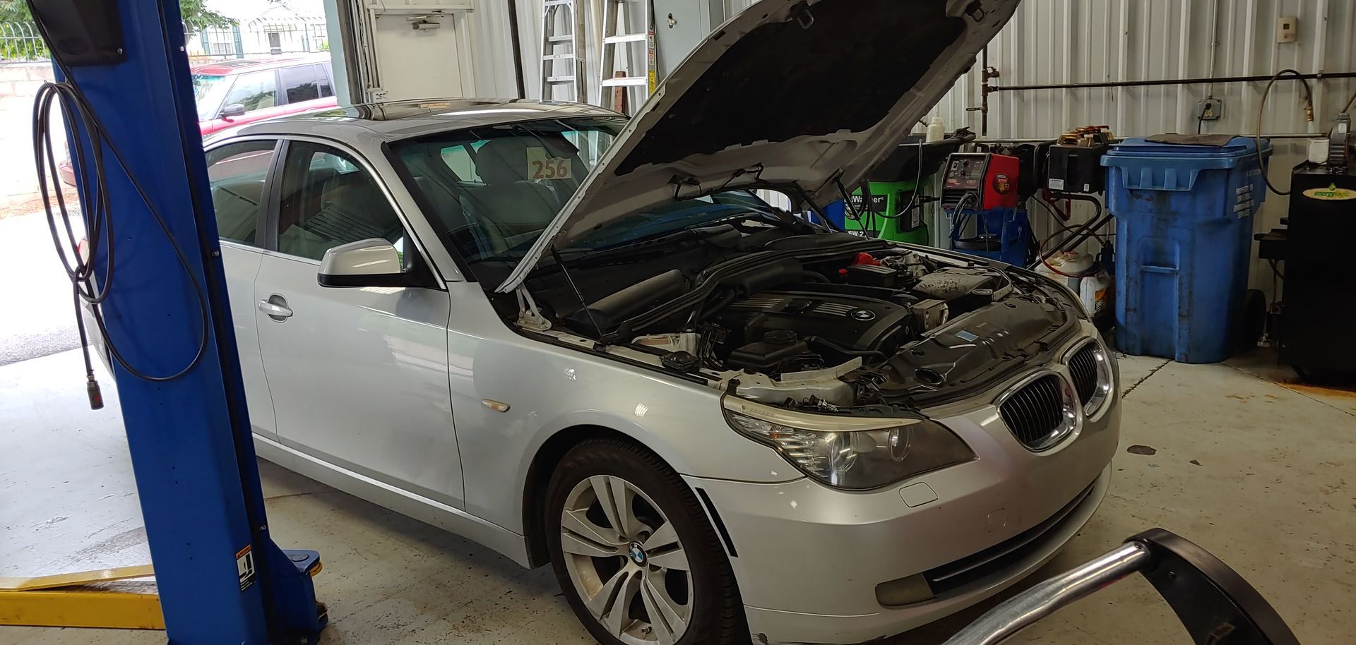 A silver car with the hood up is on a lift in a garage. | Import Specialty Service