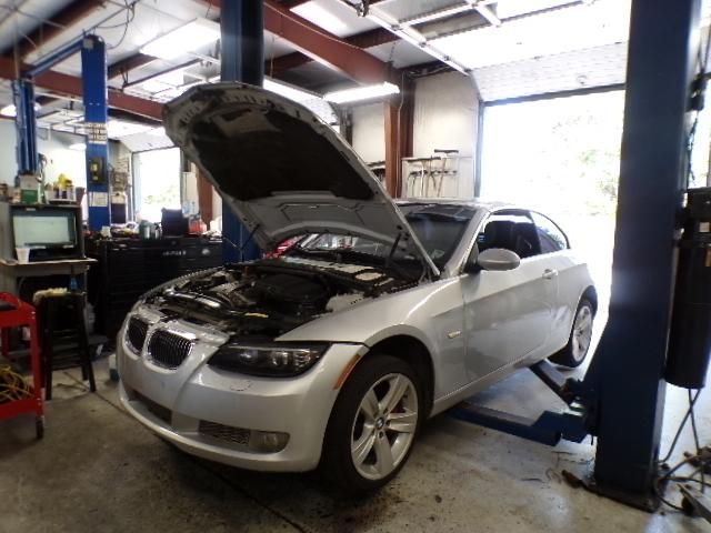 A silver car with the hood up is on a lift in a garage | Import Specialty Service