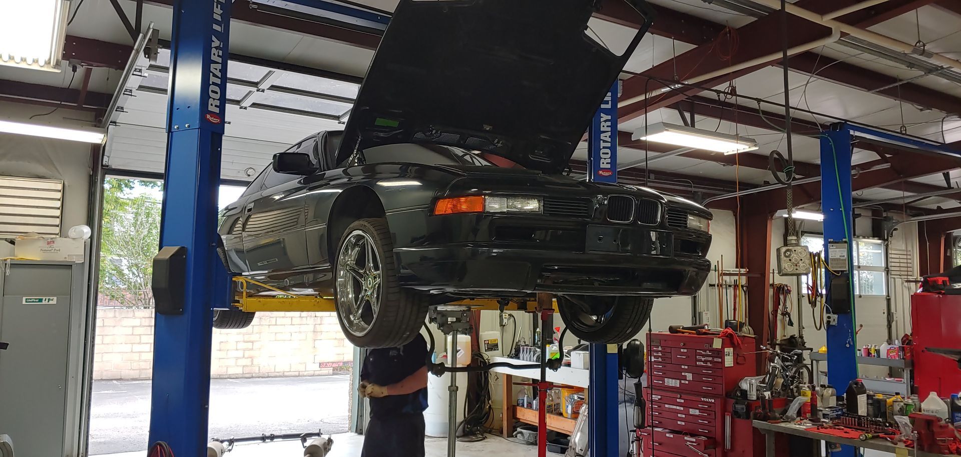 A car is on a lift in a garage with the hood up. | Import Specialty Service