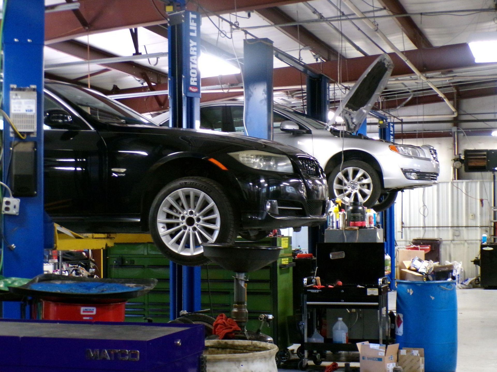 A black car is on a rotary lift in a garage | Import Specialty Service