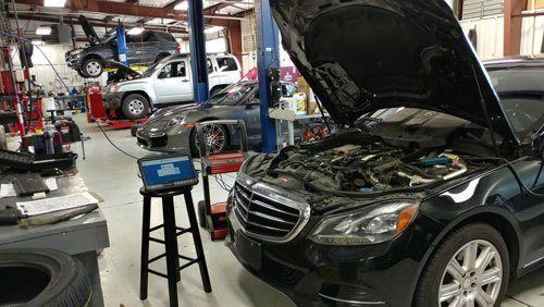 A black car with the hood up is being worked on in a garage. | Import Specialty Service