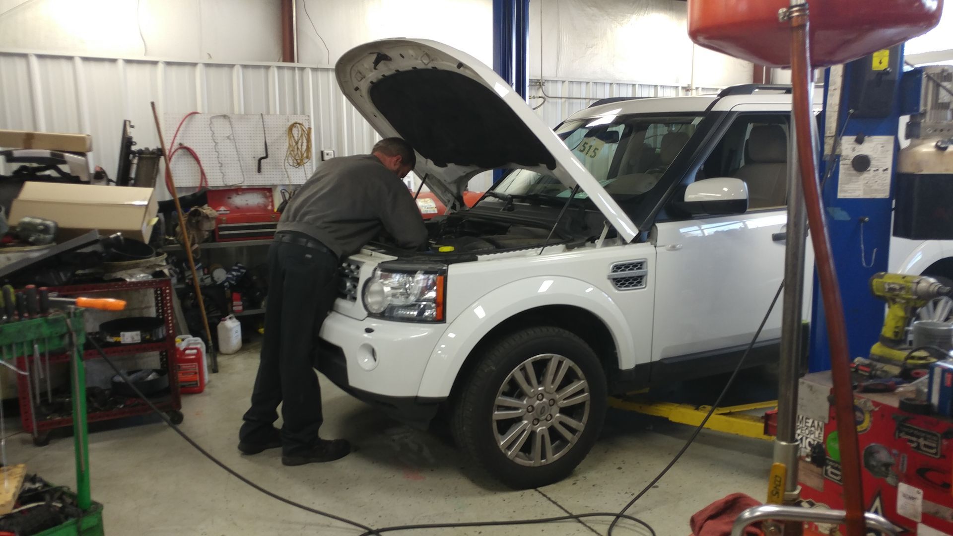A man is working on a white suv in a garage. | Import Specialty Service