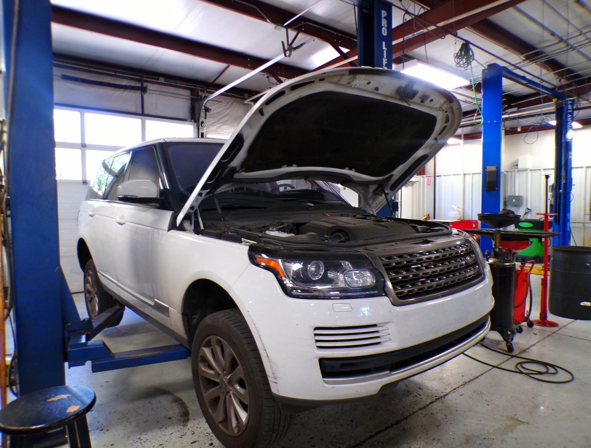 A white range rover is on a lift in a garage with its hood open. | Import Specialty Service