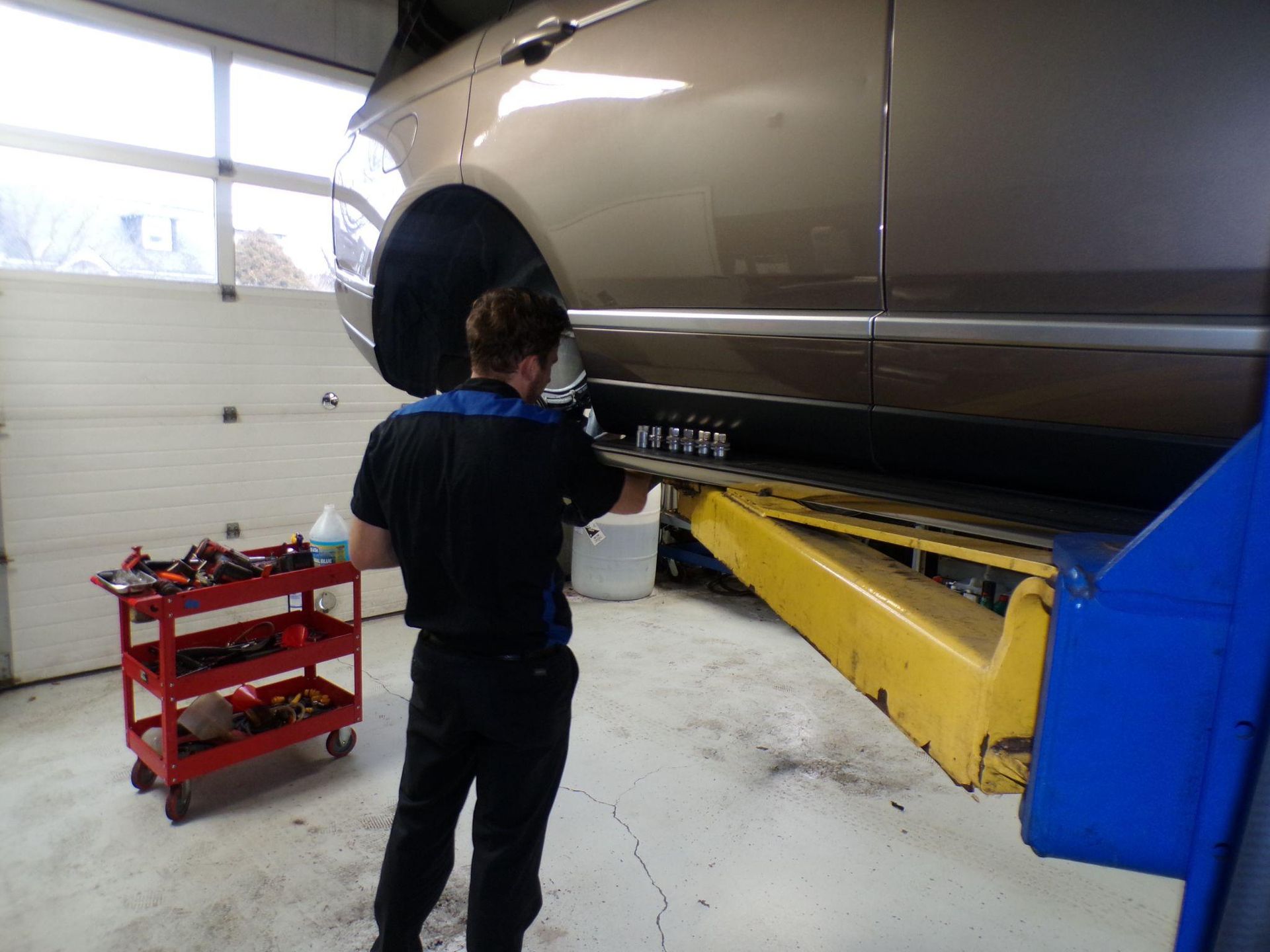 A man is working on a car on a lift in a garage. | Import Specialty Service