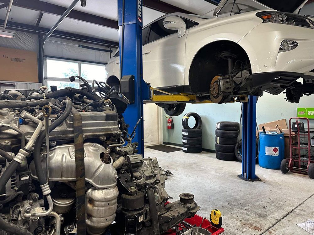 A white car is sitting on a lift in a garage. | Import Specialty Service
