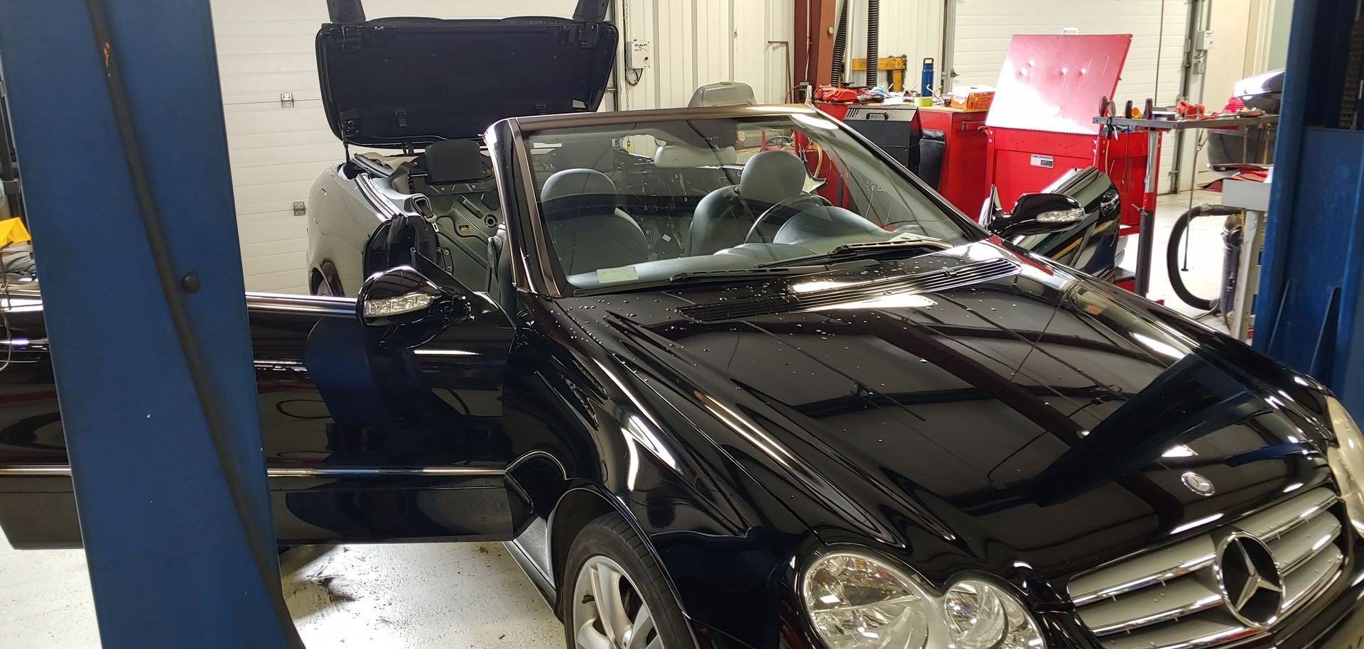 A black mercedes convertible is on a lift in a garage. | Import Specialty Service