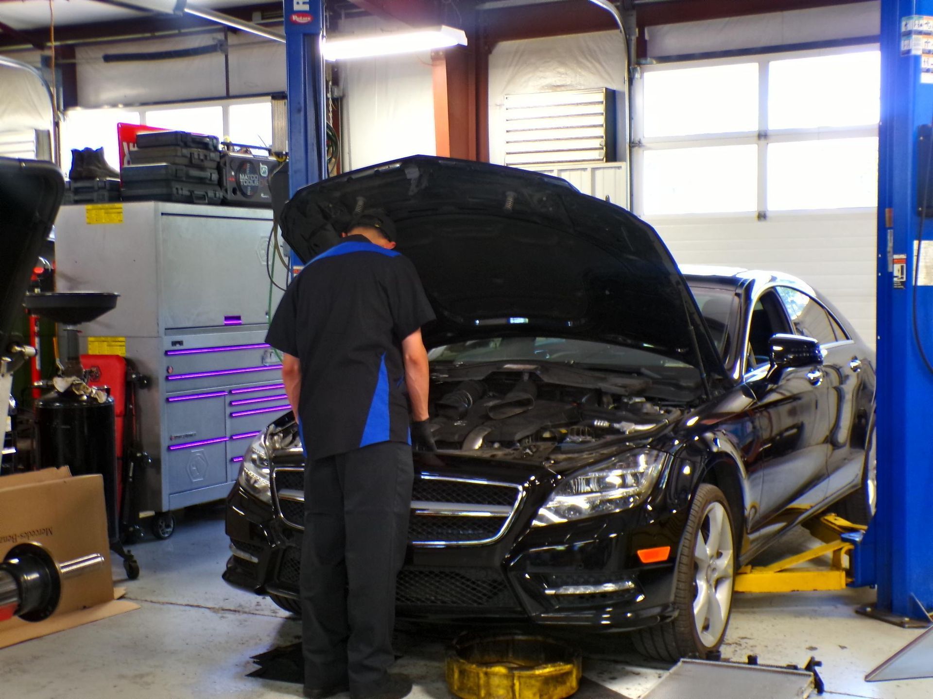 A man is working on a car in a garage with the hood up | Import Specialty Service
