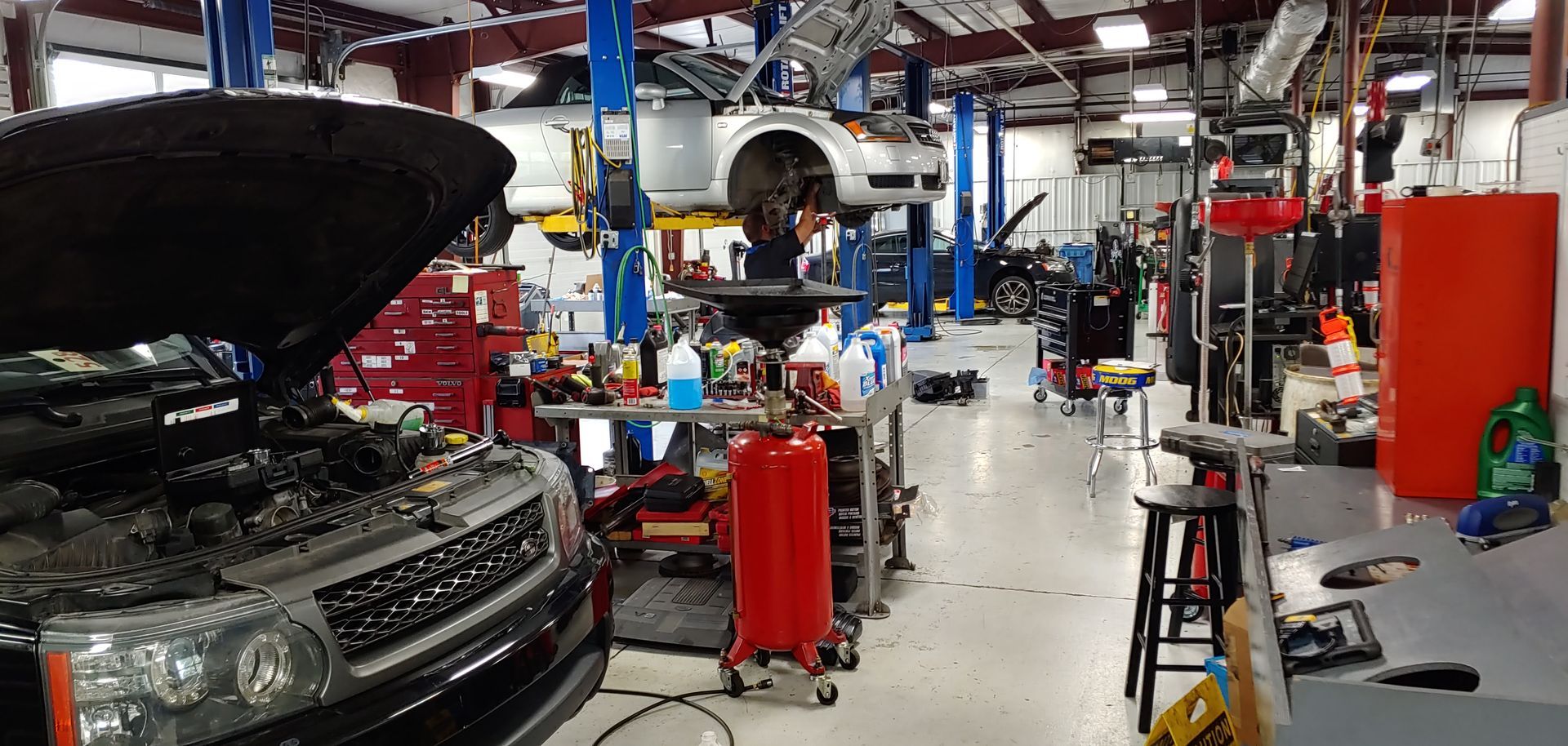 A car is being worked on in a garage with the hood up. | Import Specialty Service