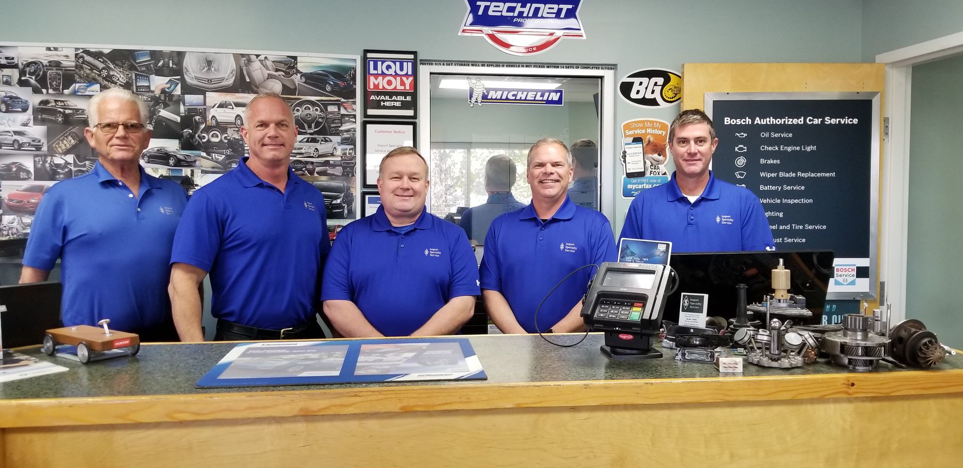 A group of men in blue shirts are standing in front of a counter. | Import Specialty Service