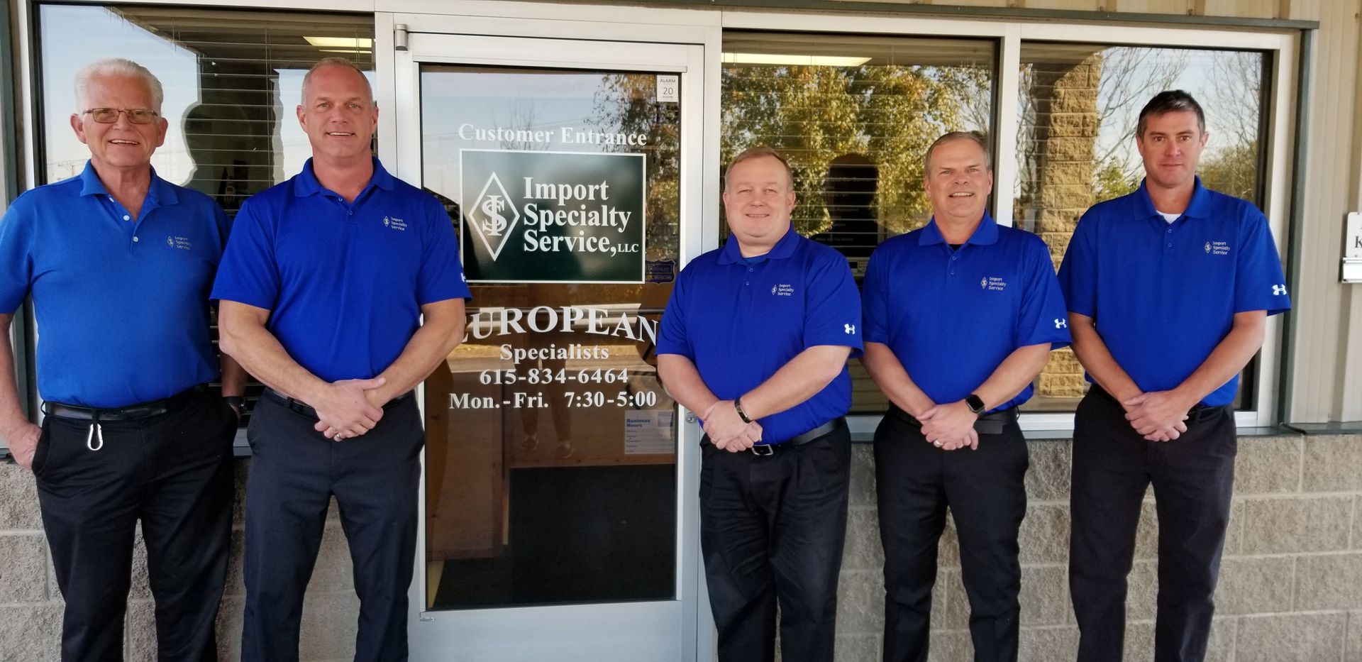 A group of men in blue shirts are standing in front of a building. | Import Specialty Service
