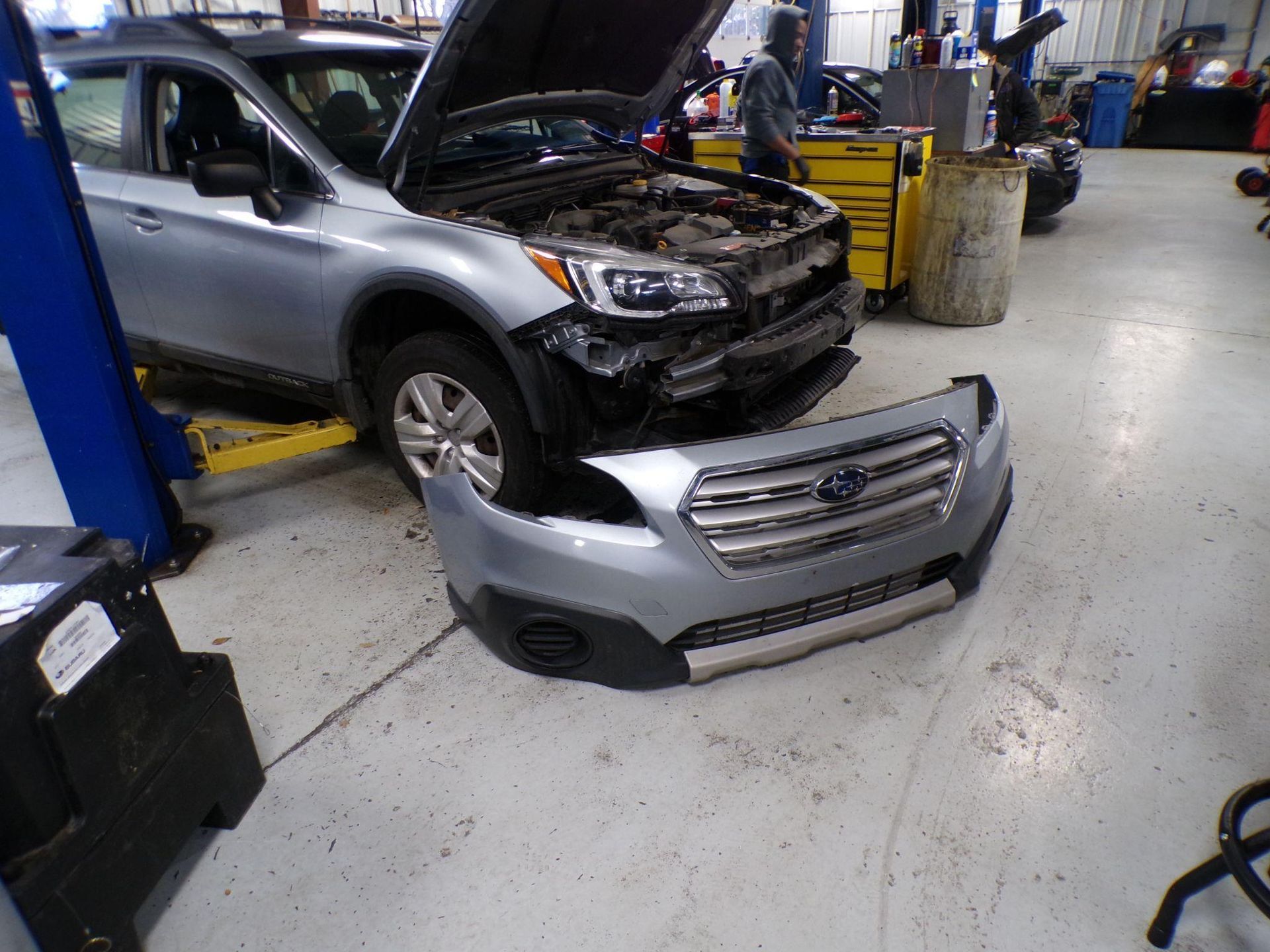 A subaru outback is being repaired in a garage with the front bumper missing. | Import Specialty Service