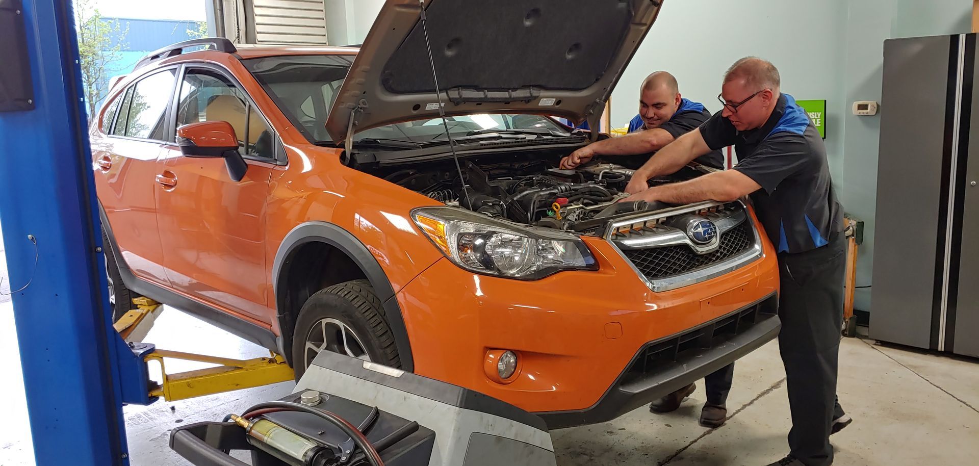 Two men are working on an orange suv in a garage. | Import Specialty Service