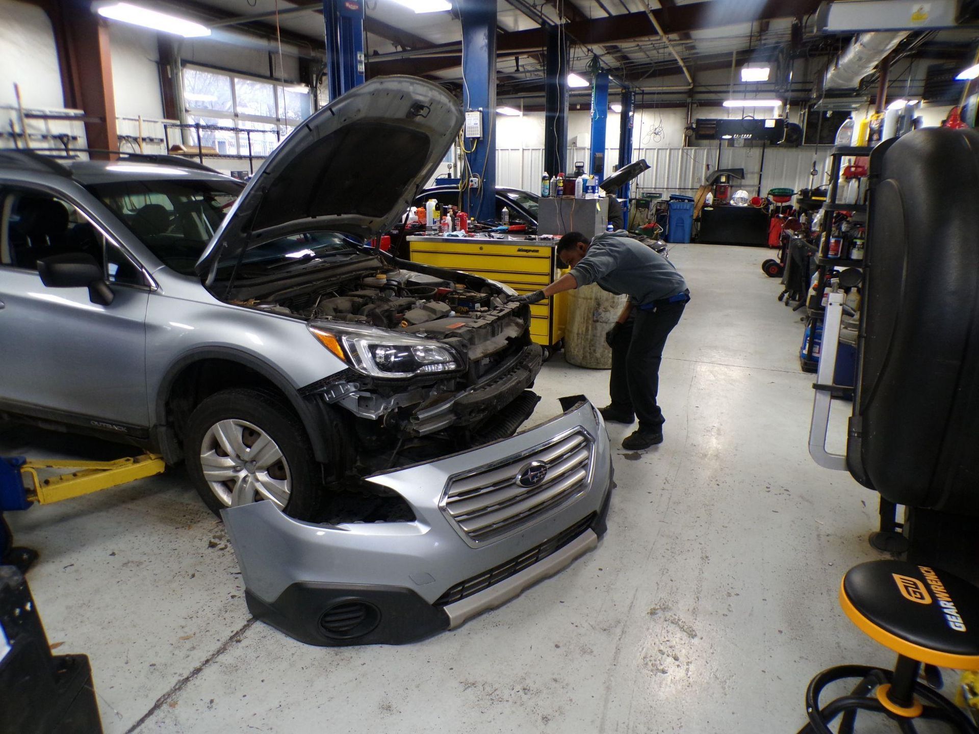 A man is working on a car in a garage with the hood open. | Import Specialty Service