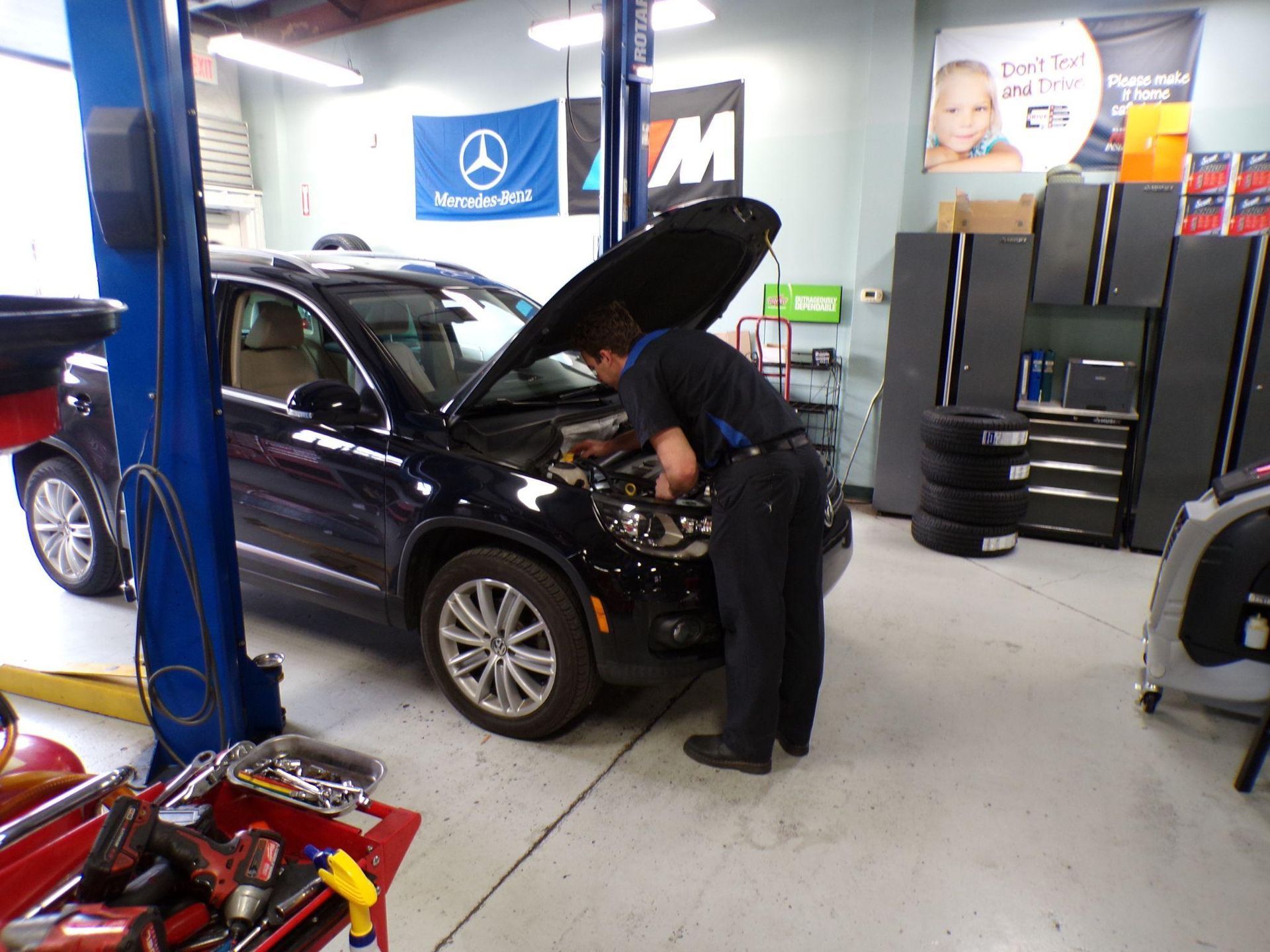 A man is working on a car in a garage with the hood up. | Import Specialty Service