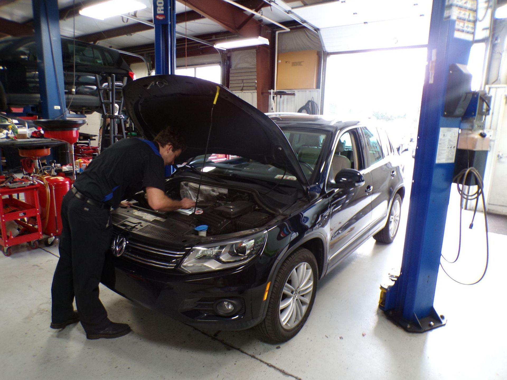 A man is working on a car in a garage with the hood open. | Import Specialty Service