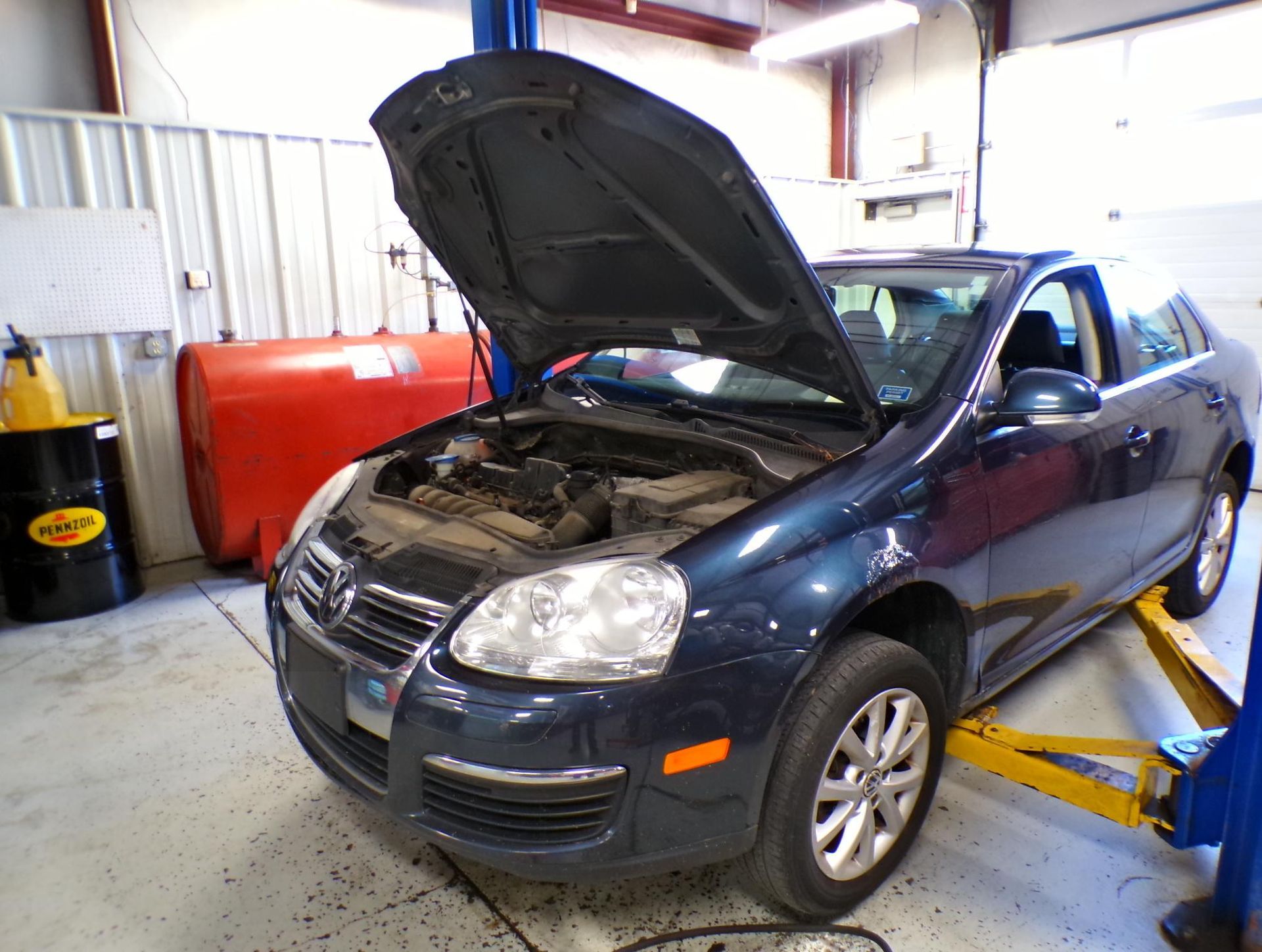 A blue car with the hood up is on a lift in a garage. | Import Specialty Service