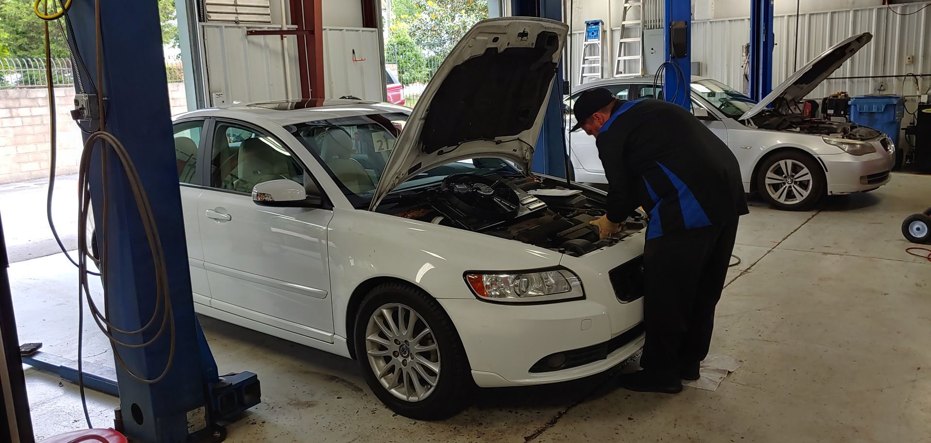 A man is looking under the hood of a white car in a garage. | Import Specialty Service