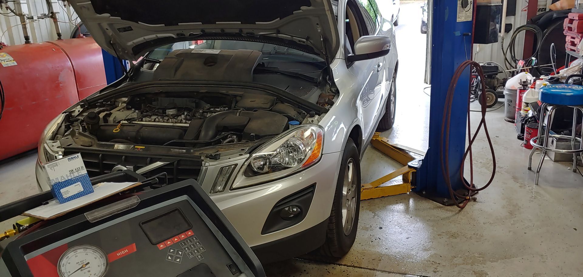 A car with the hood up is sitting on a lift in a garage. | Import Specialty Service