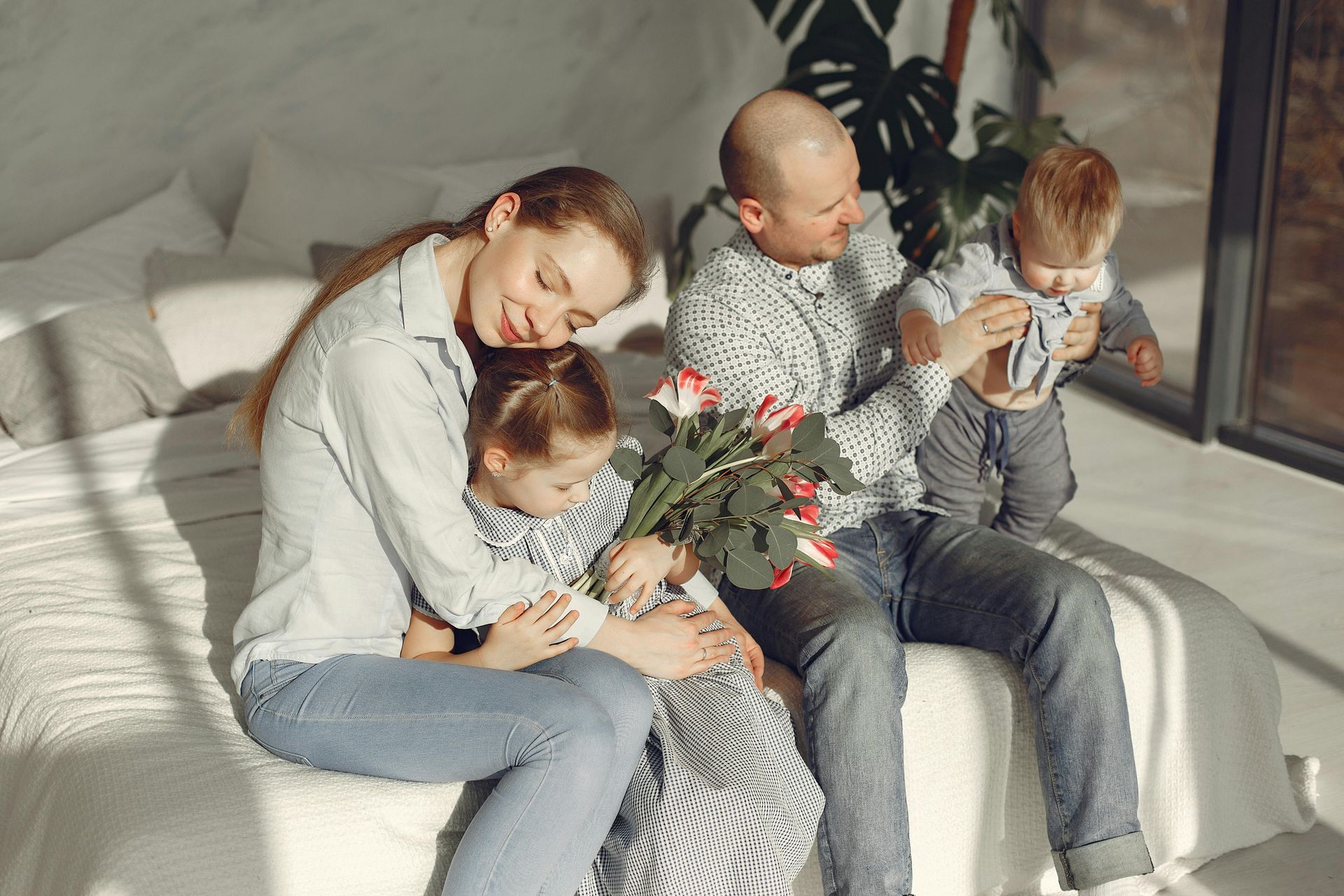 A family is sitting on a couch hugging with a bouquet of flowers.