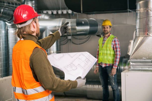 Two construction workers are standing in a room looking at a blueprint.