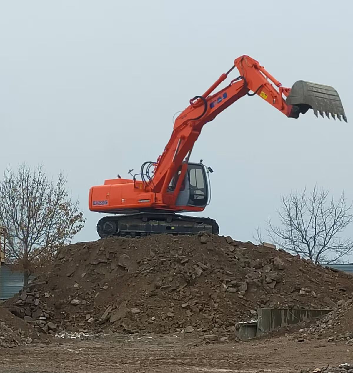 Escavatore arancione su un mucchio di terra, con il braccio alzato, pronto a lavorare. Cielo nuvoloso.