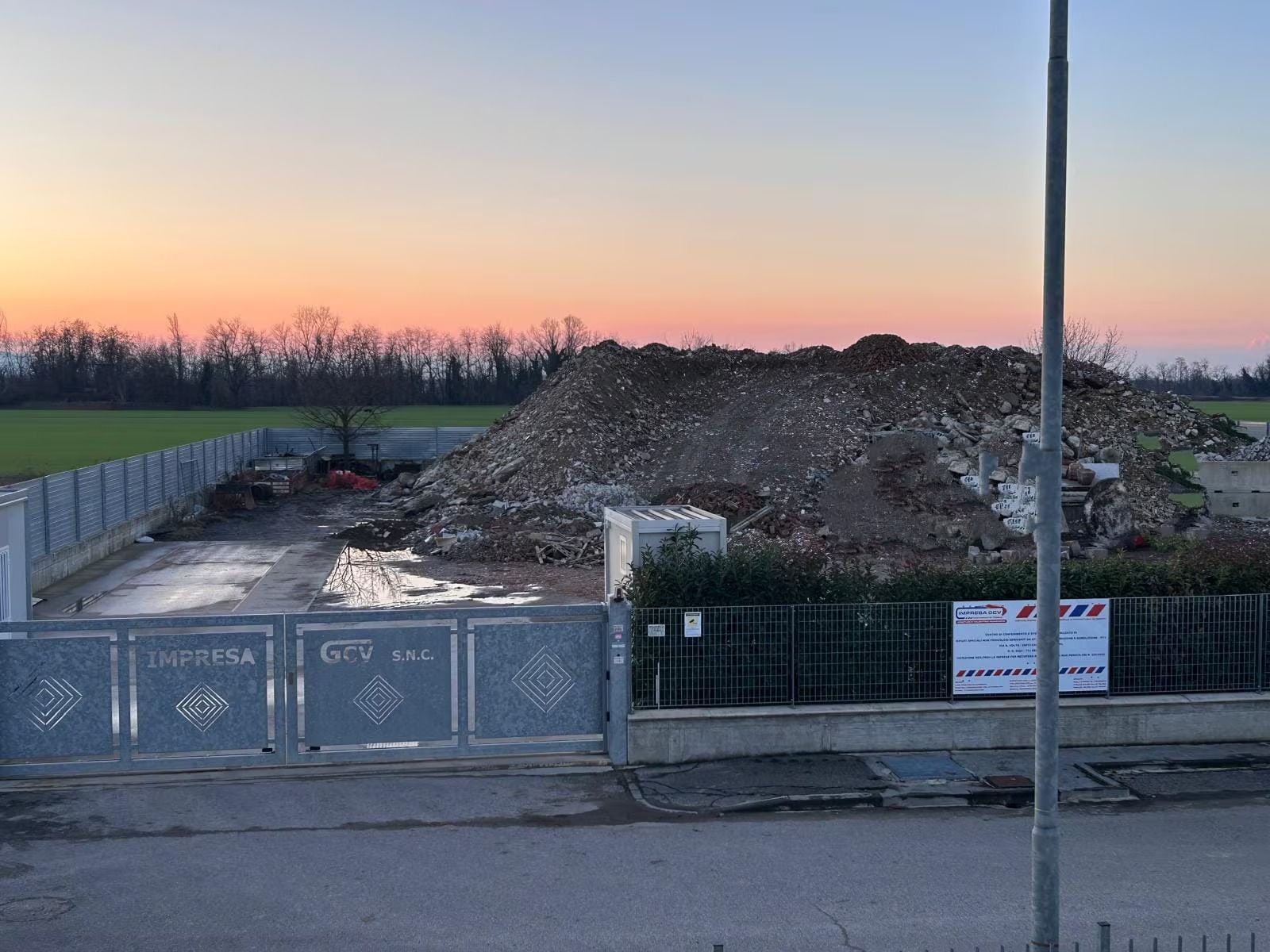 Escavatore che scava una stretta trincea lungo una strada sterrata in un campo. Cielo nuvoloso.