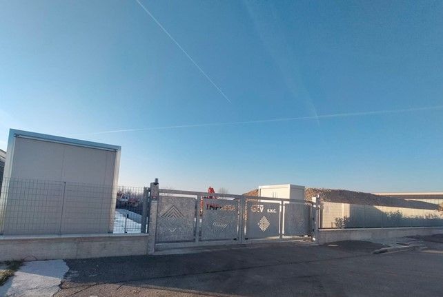 Cancello grigio davanti a un edificio sotto un cielo azzurro.