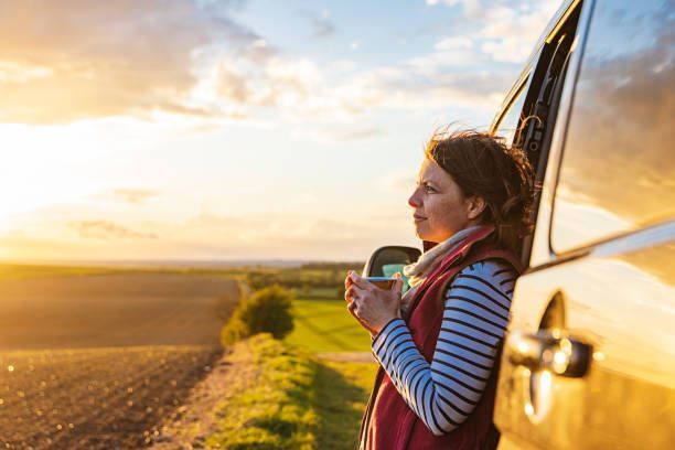 A woman is leaning out of a car window holding a cup of coffee.