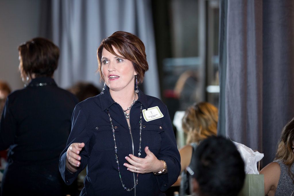 A woman in a blue jacket is giving a presentation to a group of people.