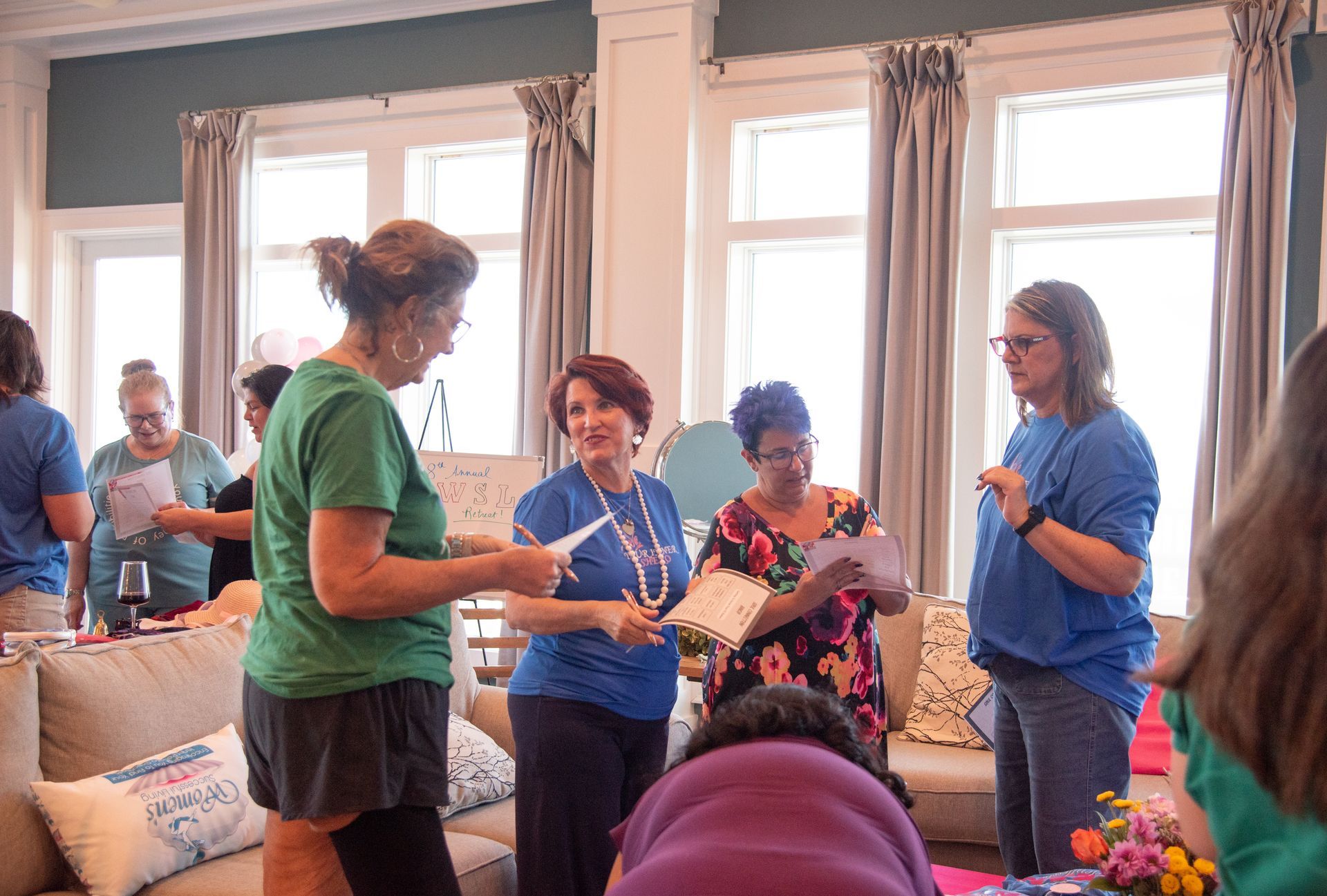 A group of women are standing in a living room talking to each other.