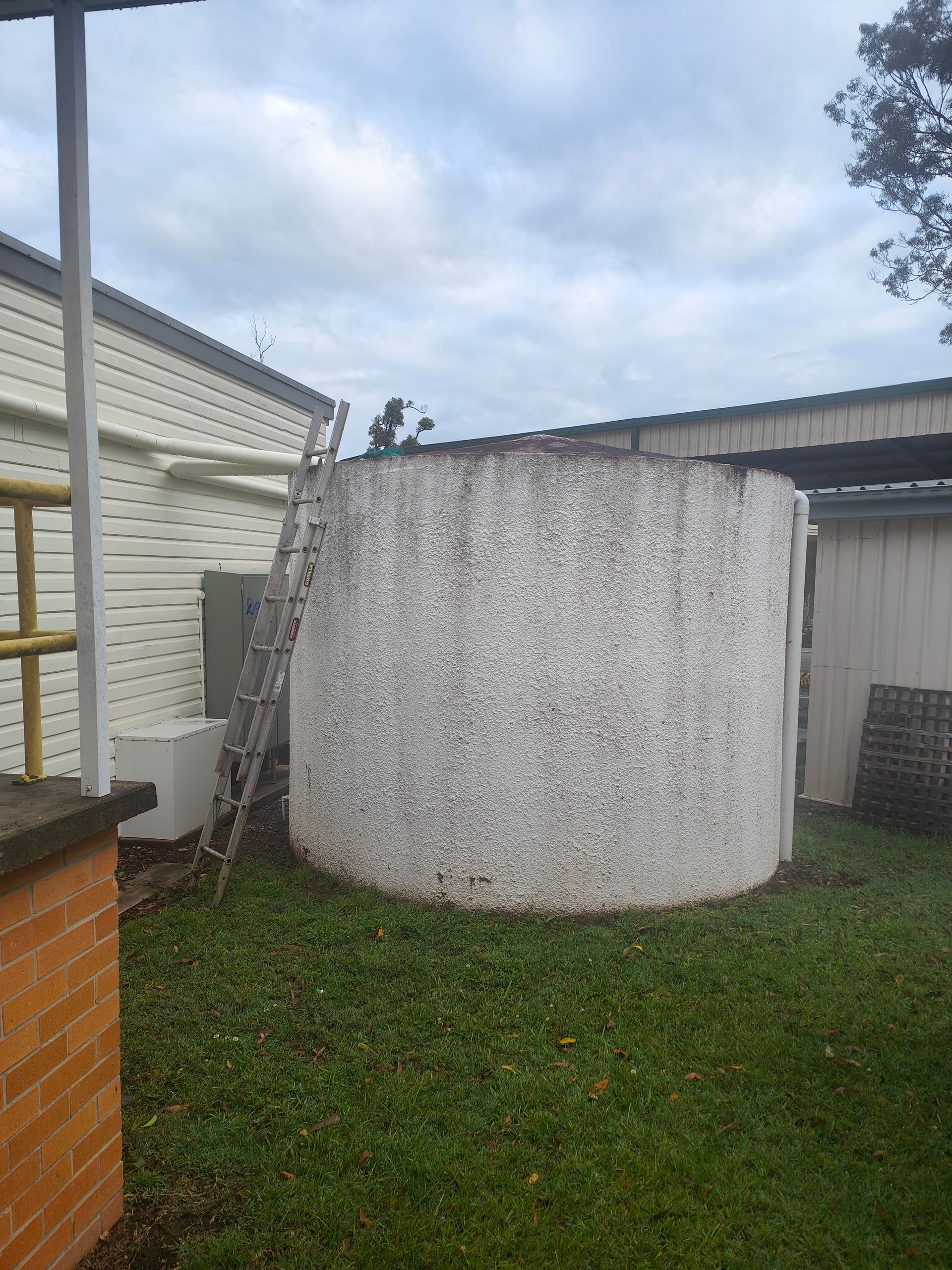 A grey concrete water tank with a ladder leaning next to it - Hastings Water Care in Port Macquarie NSW
