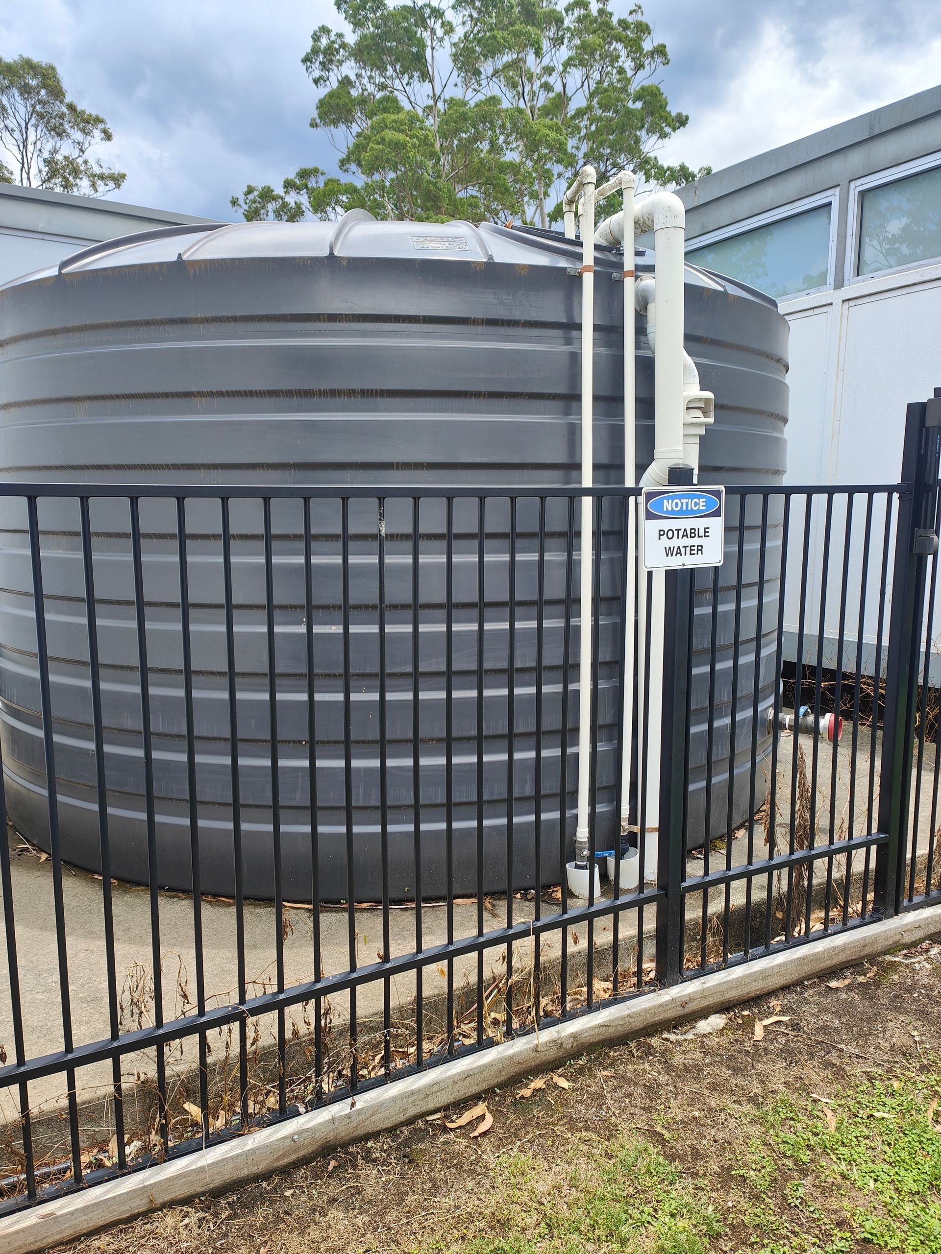 A black water tank behind a black fence with a sign - Hastings Water Care in Port Macquarie NSW