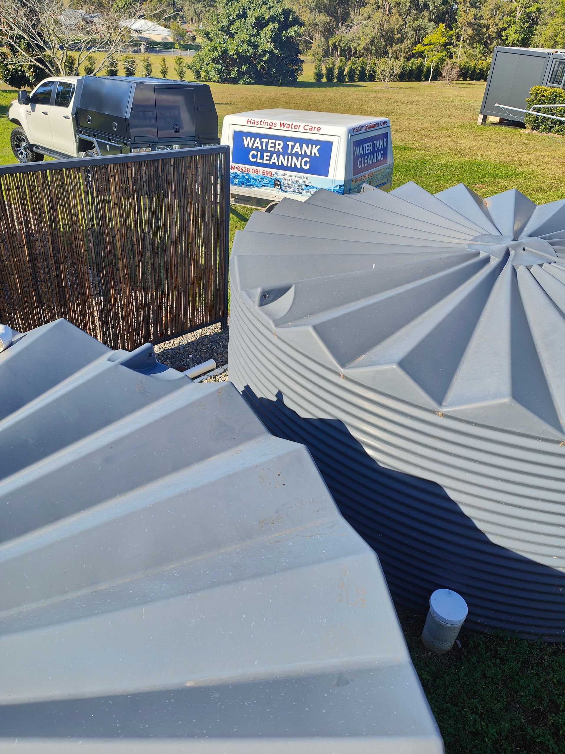 Two grey water tanks with a branded work vehicle in the distance - Hastings Water Care in Port Macquarie NSW