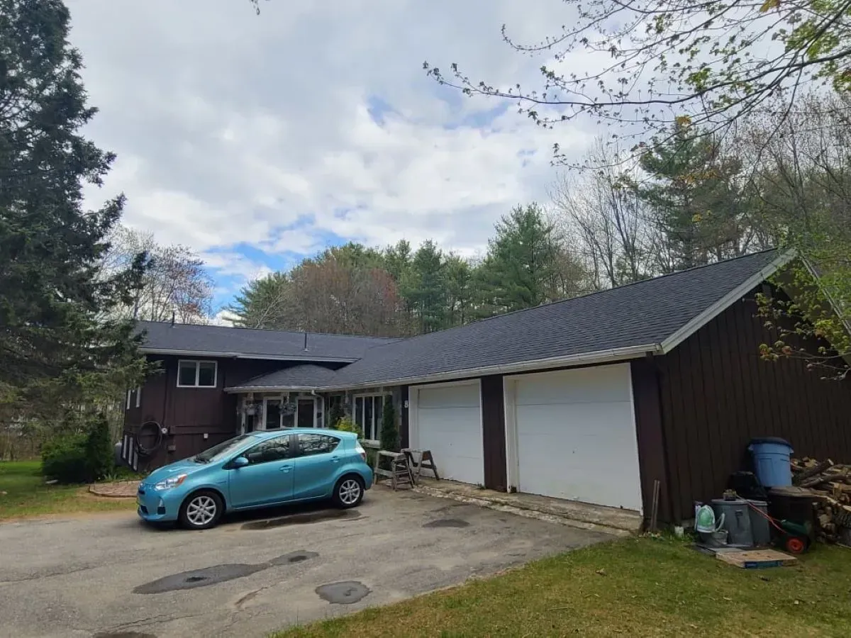 A blue car is parked in front of a house with a garage.
