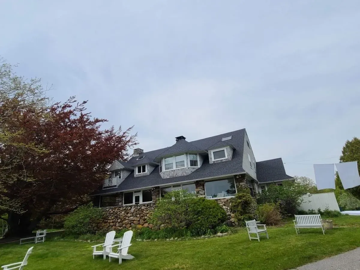 A large house with lawn chairs and a bench in front of it.