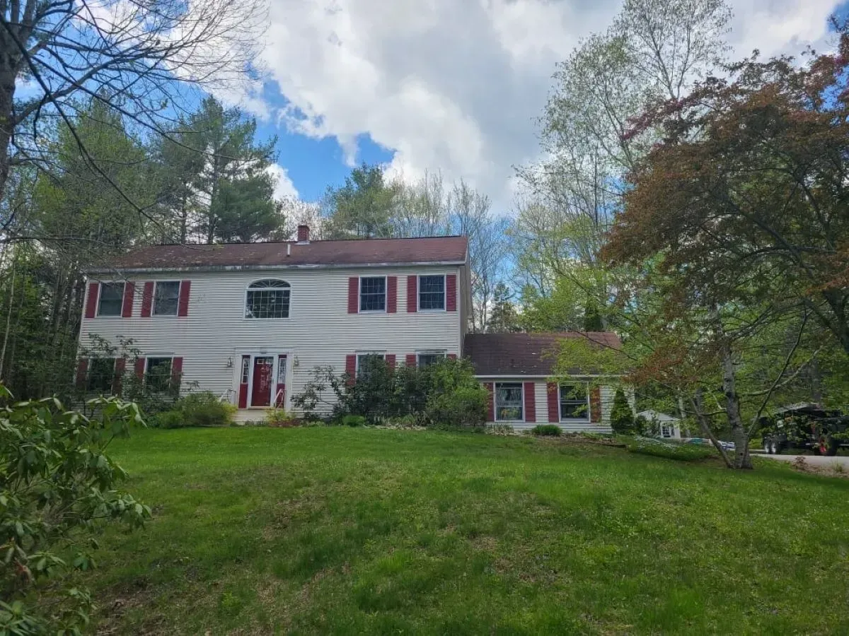 A large white house with red shutters is surrounded by trees and grass.