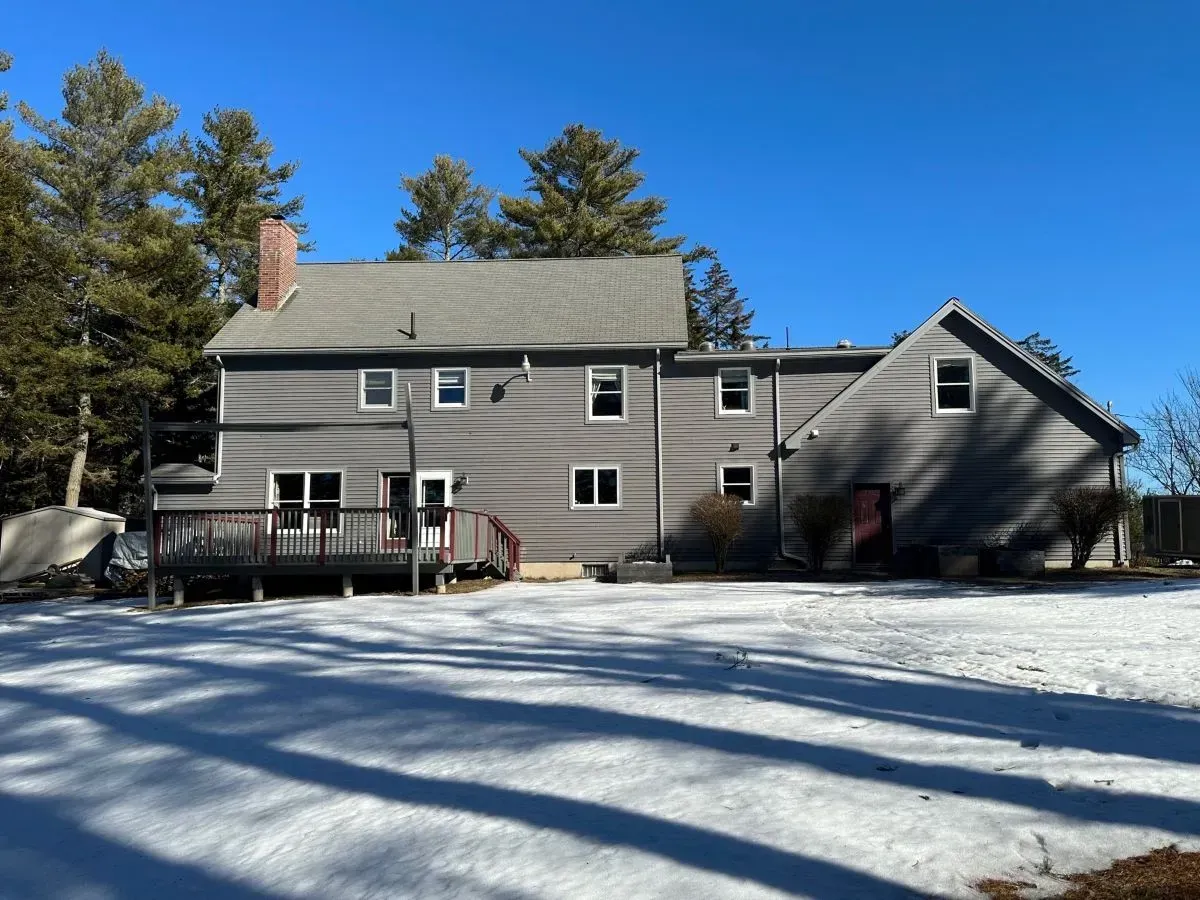 A large house with a large deck is surrounded by snow and trees.