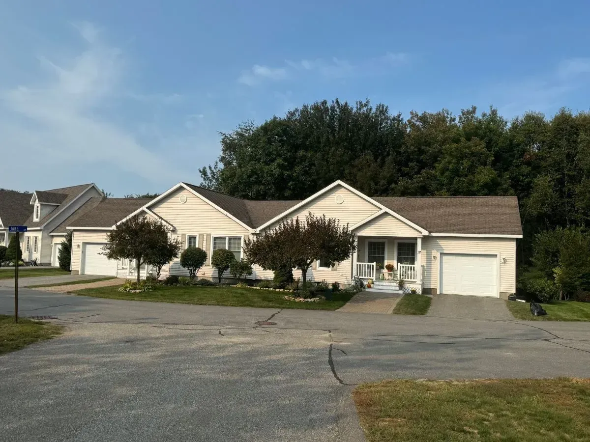 A white house with a brown roof is surrounded by trees