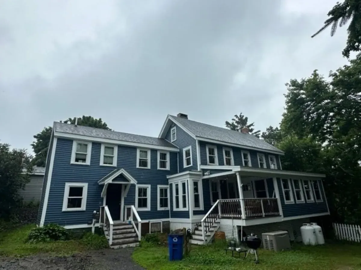 A large blue house with a porch and stairs on a cloudy day.