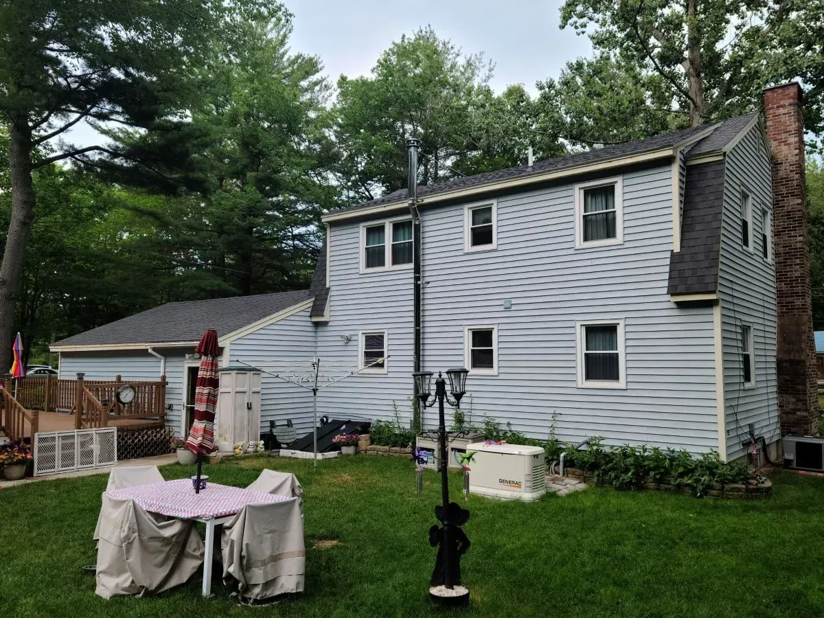 The backyard of a house with a table and chairs in the grass.