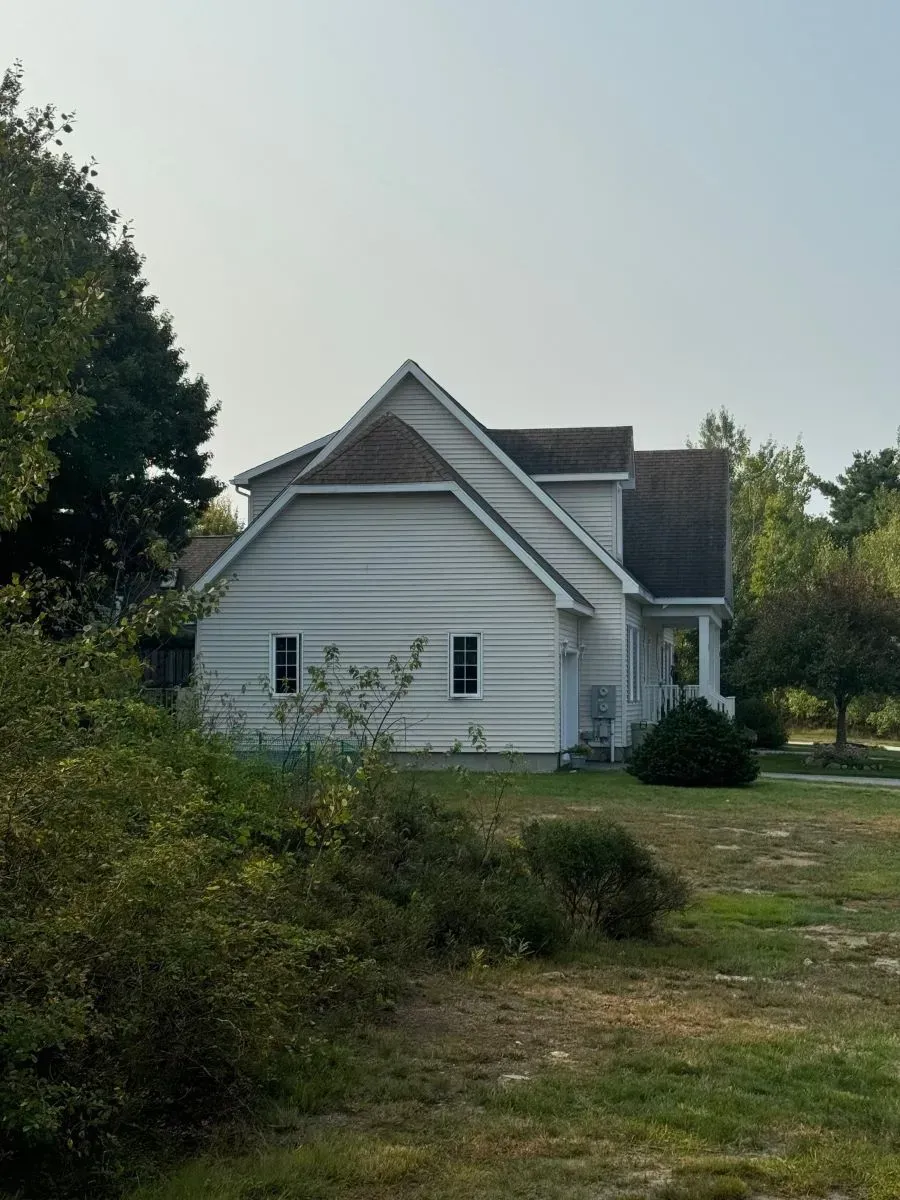 A white house with a brown roof is surrounded by trees and bushes.