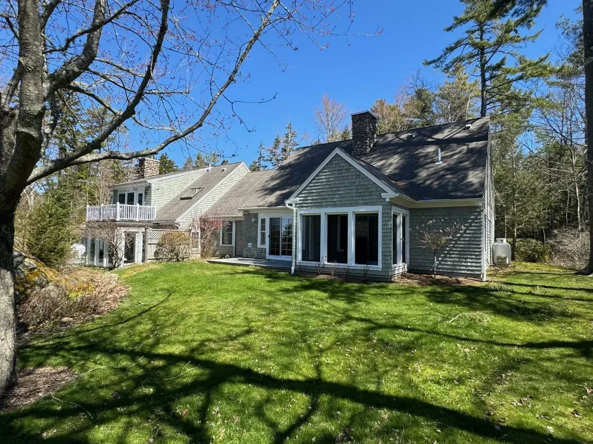 A large house with a large lawn in front of it is surrounded by trees.