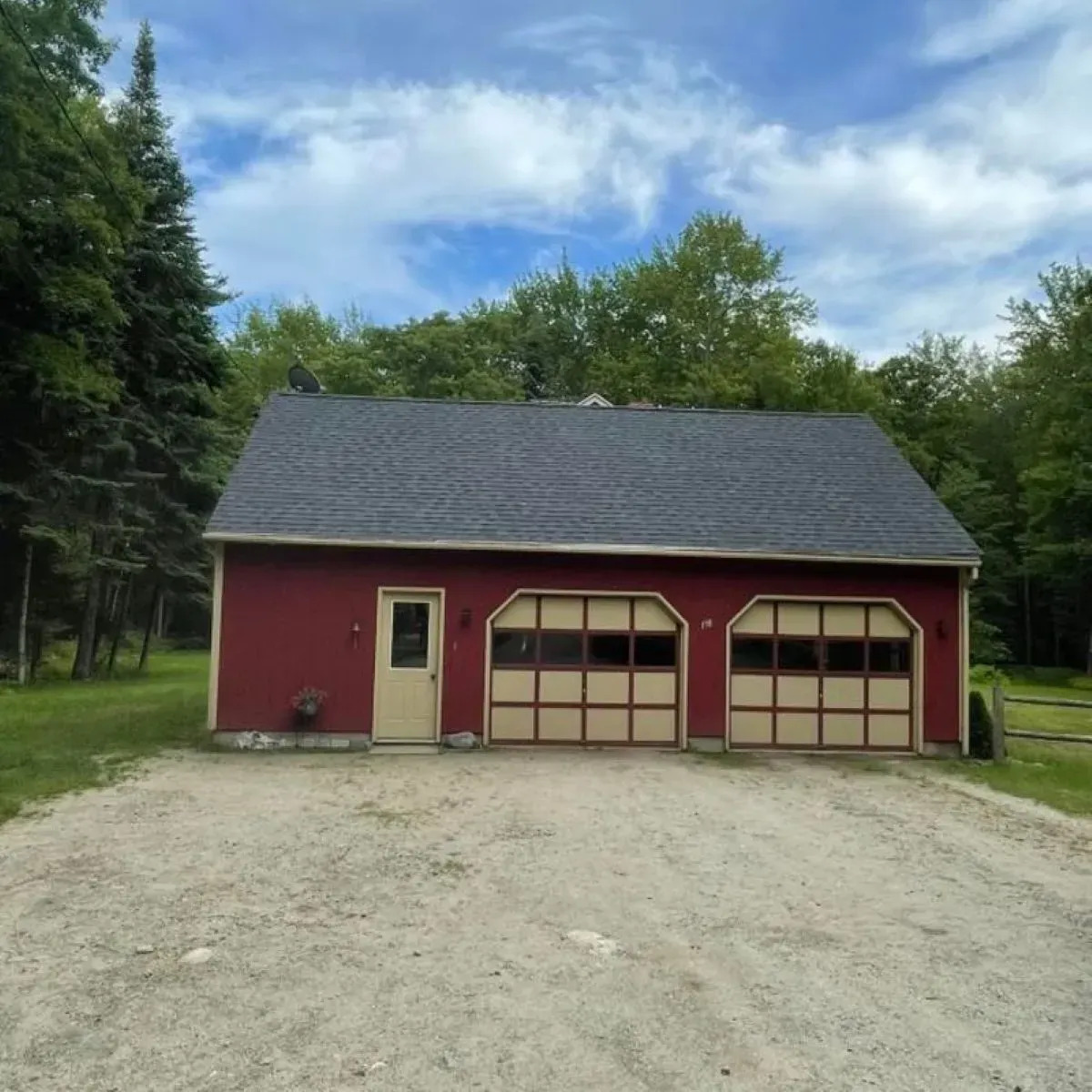 A red house with two garage doors is surrounded by trees