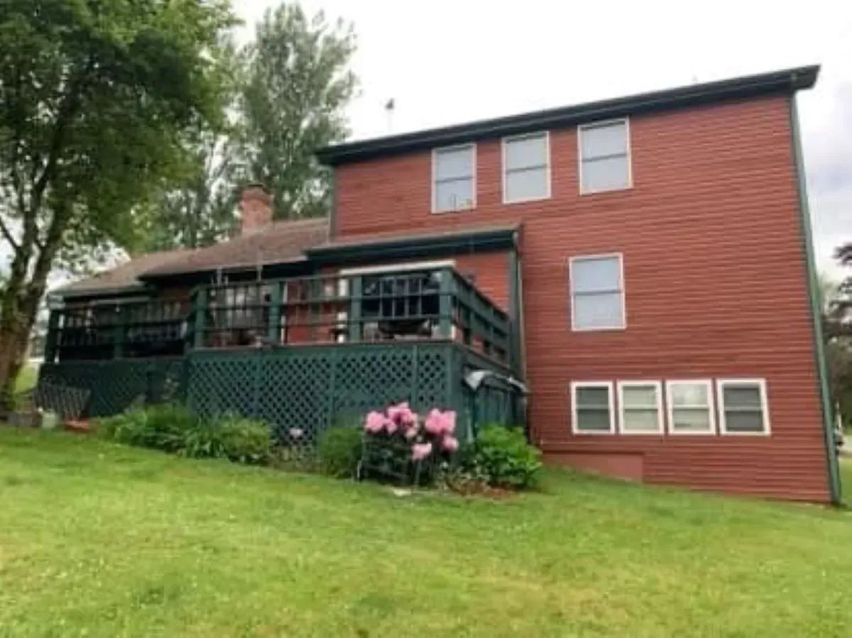 A large red brick house with a green deck is sitting on top of a lush green hill.